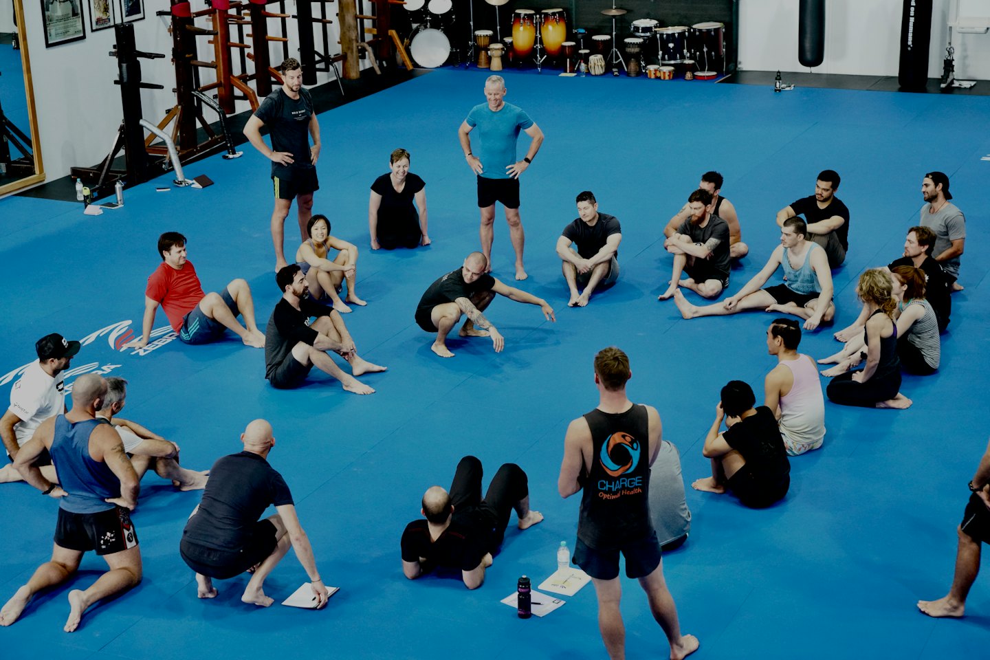 Dospelí na hodine fitnessu sa zhromaždili v kruhu na modrej podložke.